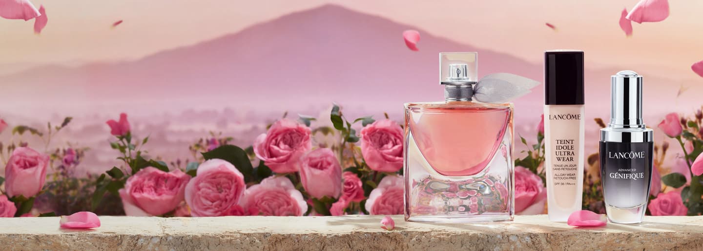 Imagen de una botella de perfume y productos de maquillaje de la marca LANCOME en un paisaje de rosas rosas. LANCOME