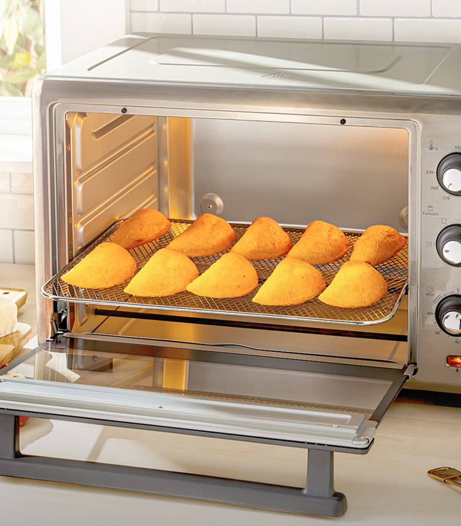 Imagen de un horno electrico plateado de la marca OSTER, dentro de el estan unas empanadas. OSTER
