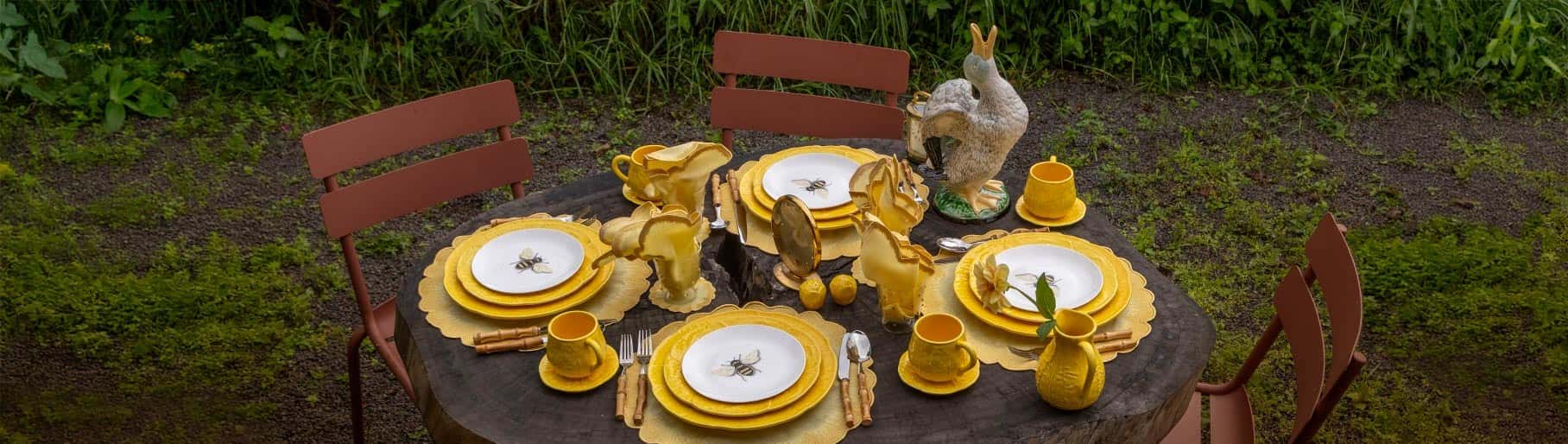 imagen de una mesa acomodada con m,anteles y una vajilla color blanca con orillas amarillas de la marca ZASH en un jardin