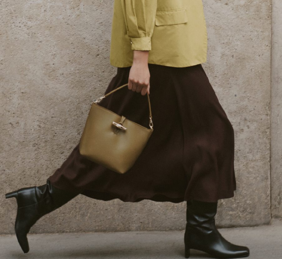 Imagen de mujer falda cafe, blusa verde y bolso verde. LONGCHAMP.