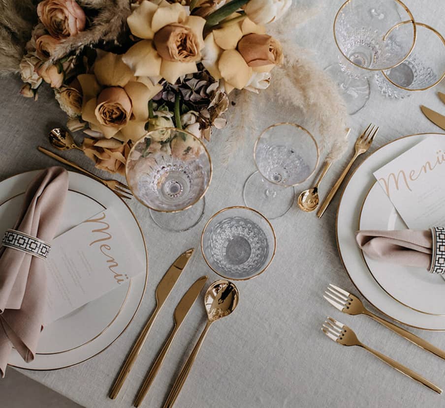 Imagen una mesa acomodada con vajilla de lujo blanca con toques dorados copas y cubiertos de color dorado, MESA Y BAR