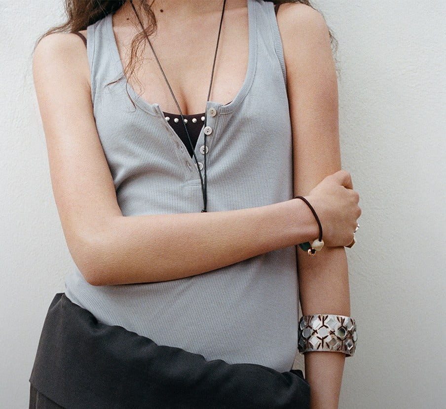 mujer con blusa gris, pantalon negro y joyeria plateada de la marca MANGO