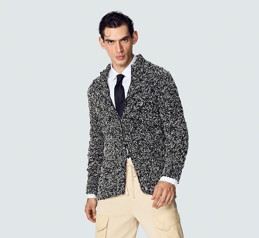 imagen de hombre usando camisa blanca, corbata negra, pantalon beige y sueter negro con blanco de la marca EPSILON