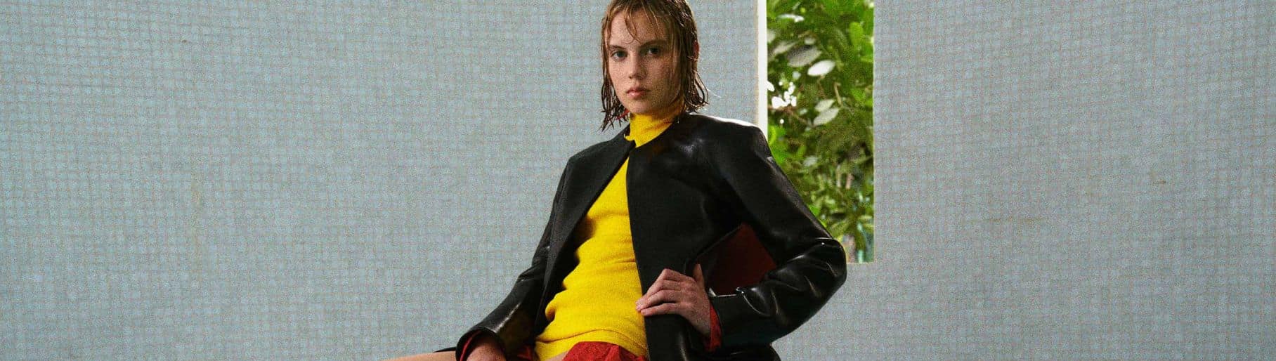 Imagen de mujer con vestido amarillo, chamarra negra, zapatillas negras  y bolso negro de la marca LOEWE