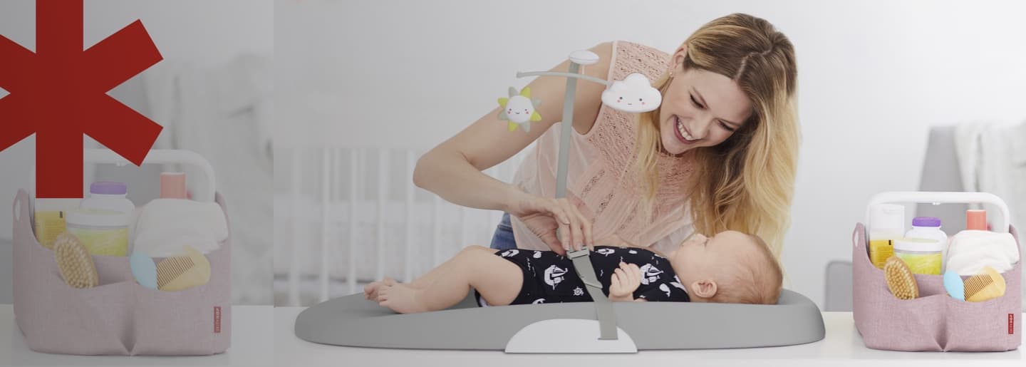 Imagen de una madre sonriendole a su bebe, el bebe se encuentra sobre un cambiador de la marca. SKIP HOP