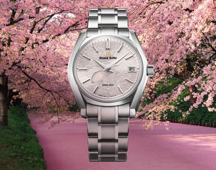 imagen de un reloj plateado, con caratula rosa en un fondo con cerezos y un camino de asfalto rosa
