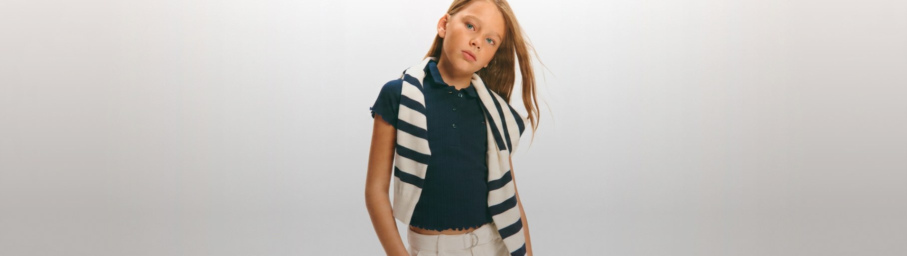 imagen de niña con sueter a rayas blanco con negro, blusa verde y pantalon blanco de la marca TOMMY HILFIGER