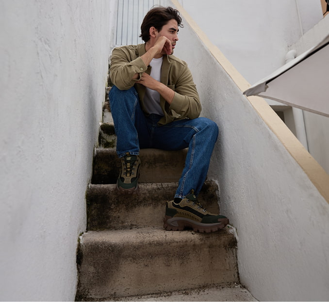 Hombre sentado en escaleras con playera verde pantalon azul y botas CATERPILLAR