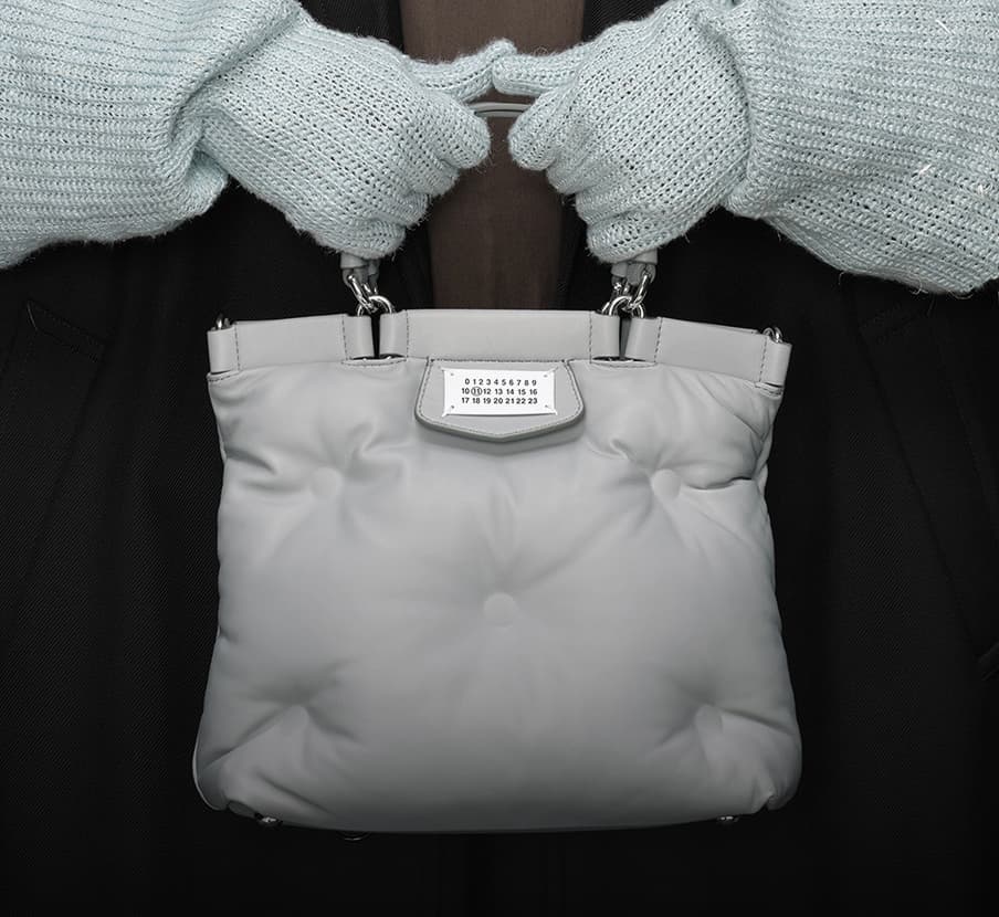 imagen de unas manos con guantes blancos tegidos sosteniendo un bolso gris claro de la marca MAISON MARGIELA