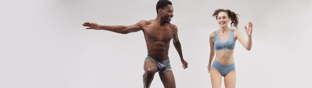 Imagen de un hombre y una mujer con ropa interior, el lleva boxer de licra color gris y ella top y panti color azul. SKINY