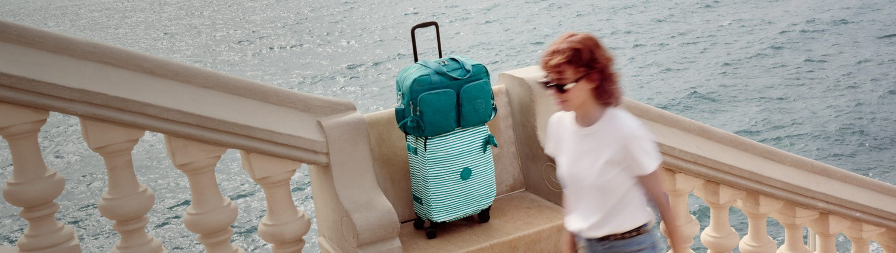 imagen de mujer junto a maleta verde con blanco de la marca KIPLING