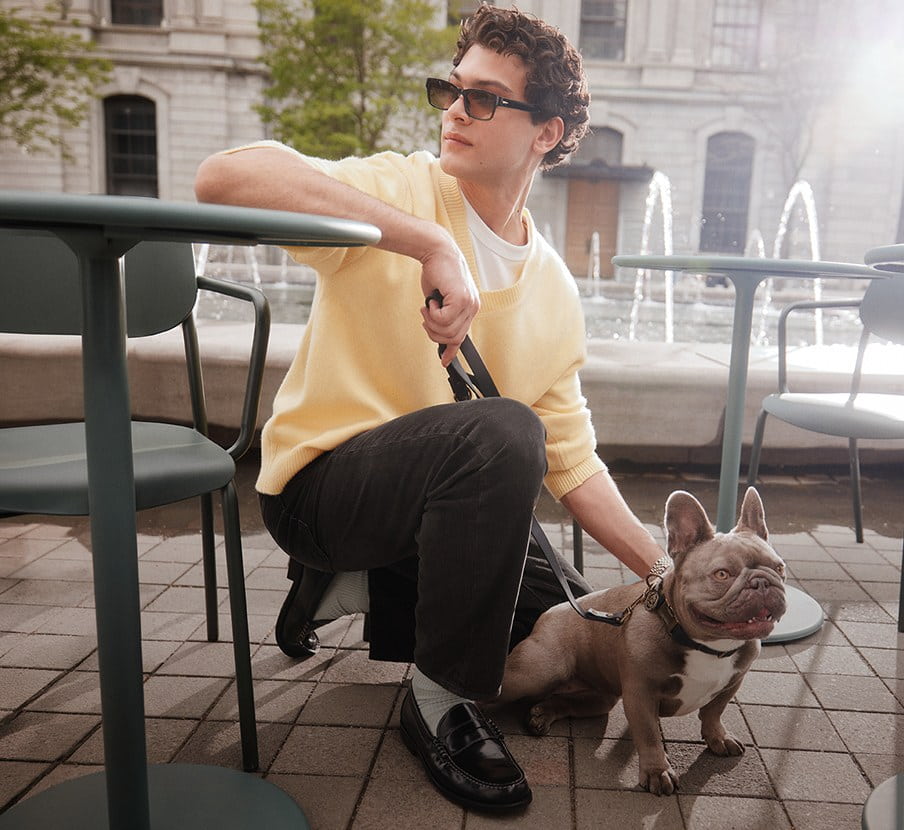 Imagen de un hombre acarisiando a su perro, el viste un sueter color amarillo claro y pantalon color negro de la marca ALDO