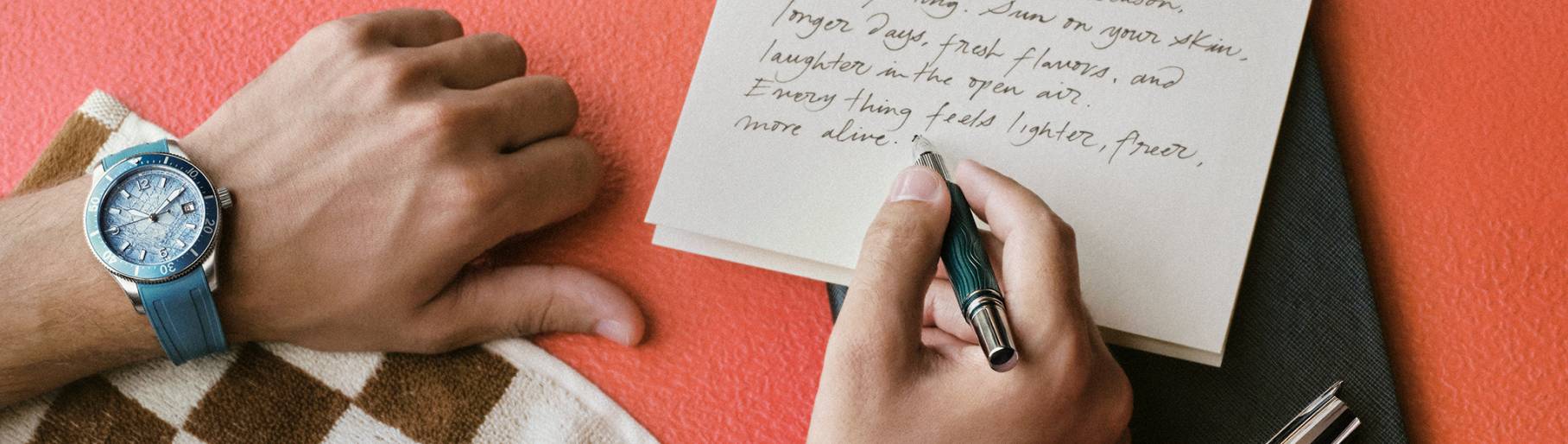 Imagen de los brazos de un hombre escribineedo una carta, en su brazo izquierdo lleva un reloj plateado con azul, MONTBLANC