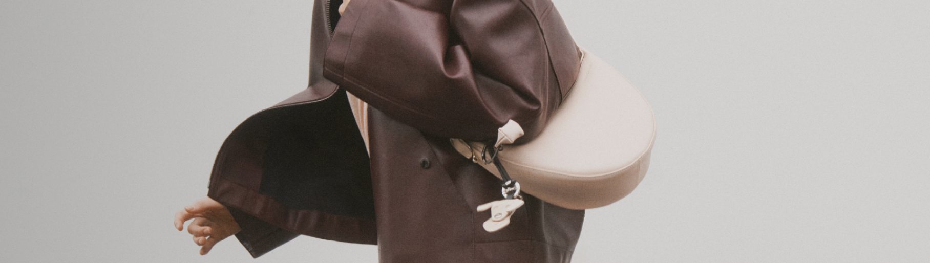 Imagen de mujer con chamarra cafe y bolso blanco. LONGCHAMP.