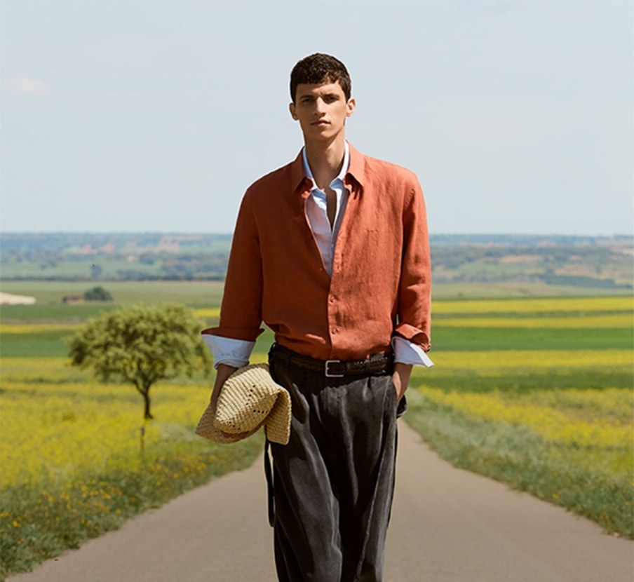 imagen de hombre caminando con chamarra cafe y pantalon gris de la marca ADOLFO DOMÍNGUEZ