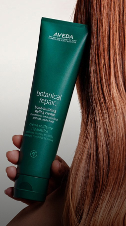imagen de mujer de espalda sosteniendo botella de crema para peinar botanical-repair  de la marca AVEDA