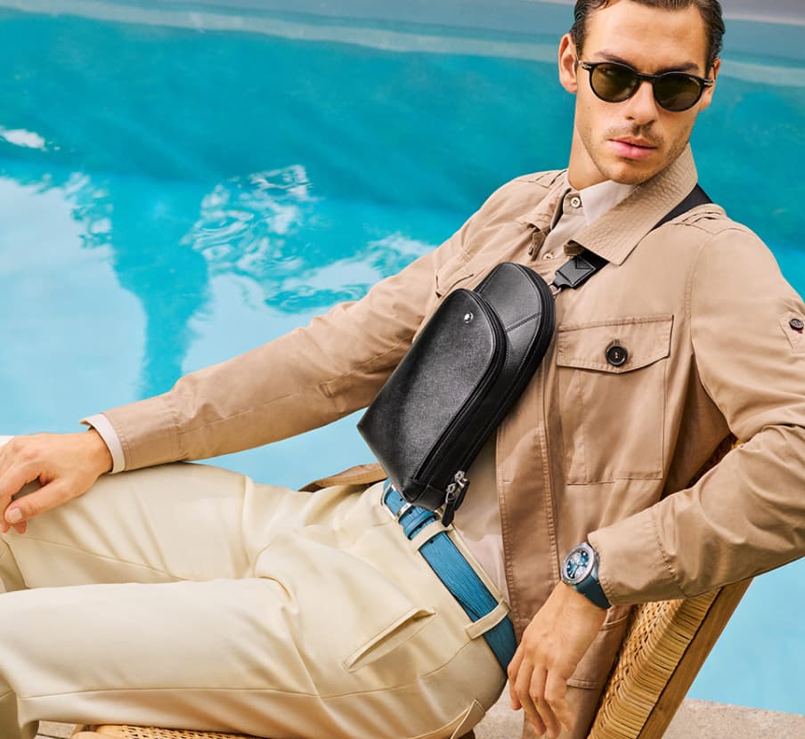 Imagen de un hombre sentado en un camastro, lleva ropa beige y una mochila crossbody lateral, MONTBLANC