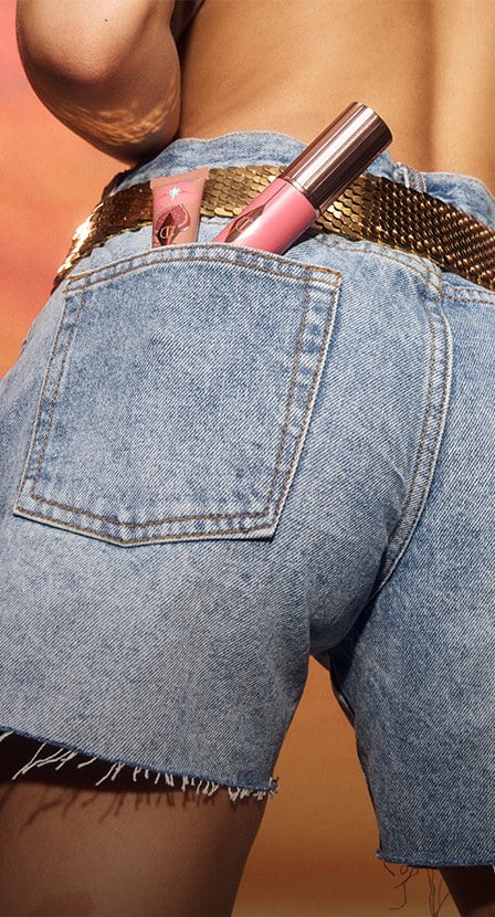 imagen de mujer de espaldas, usando short de mezclilla, en la bolsa trasea lleva un maquillaje de la marca CHARLOTTE TILBURY