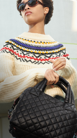 imagen con sueter tejido color hurdo y con detalles de colores en el cuello sosteniendo un bolso negro de la marca MZ WALLACE