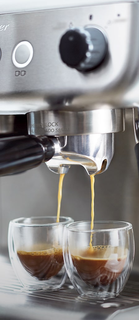 Imagen de una cafetera expres de la marca OSTER, color plateada con dos vasos pequeños llenandose de cafe. OSTER
