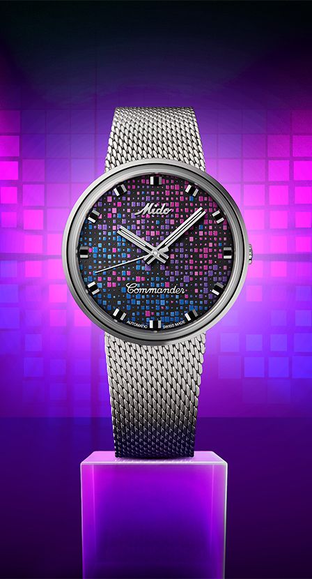 reloj plateado circular, en la caratula de color negra lleva muchos cuadritos de colores rosas morados y azul de la marca MIDO