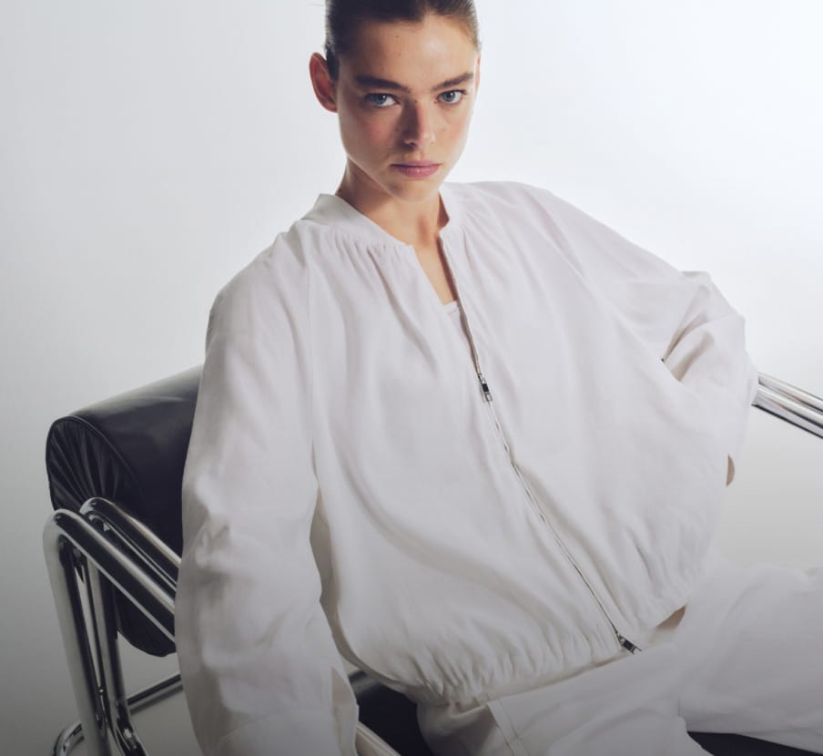 Imagen de una mujer sentada en una silla color negra, lleva ropa color blanca, Mujer