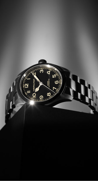 Imagen de reloj plateado con caratula negra, manecillas y numerales blancos, HAMILTON