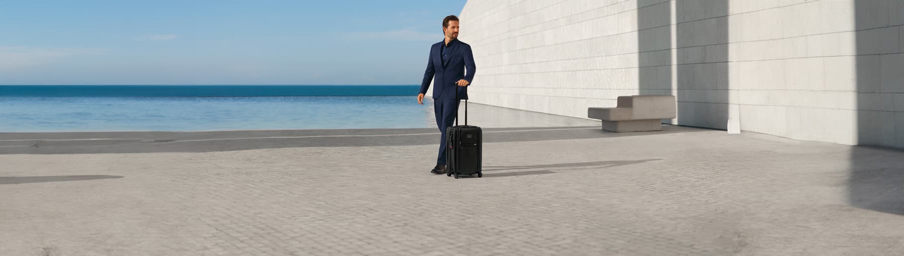 Hombre usando traje azul junto a maleta negra TUMI