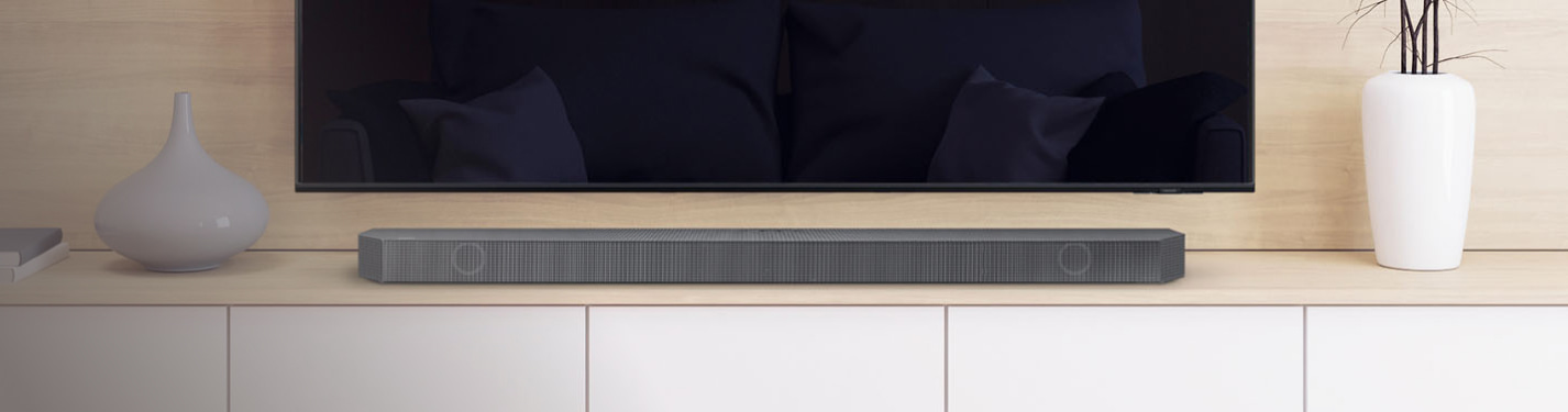 imagen de una barra de sonido color gris sobre un mueble blanco en un fondo de madera