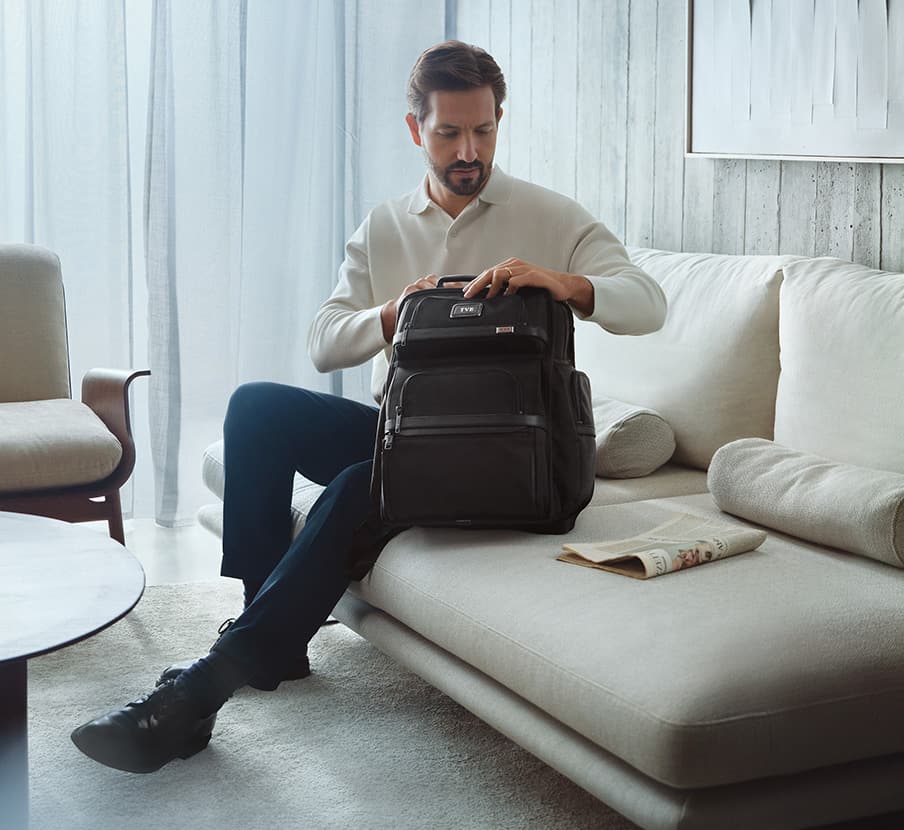 Imagen de hombre con camisa blanca pantalon azul y machila negra TUMI